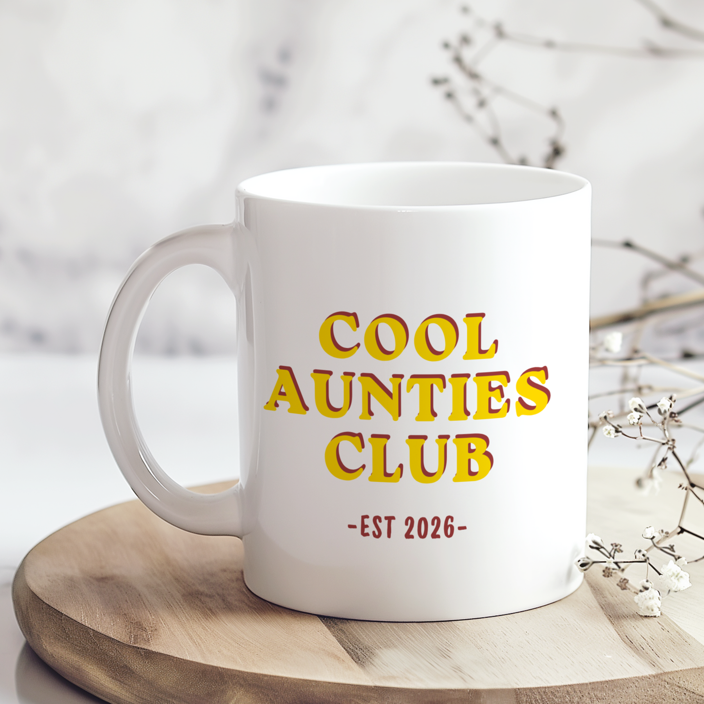 White ceramic mug featuring “Cool Aunties Club EST 2026” retro style typography in yellow and red colours, displayed on a neutral wooden background with minimalist styling.