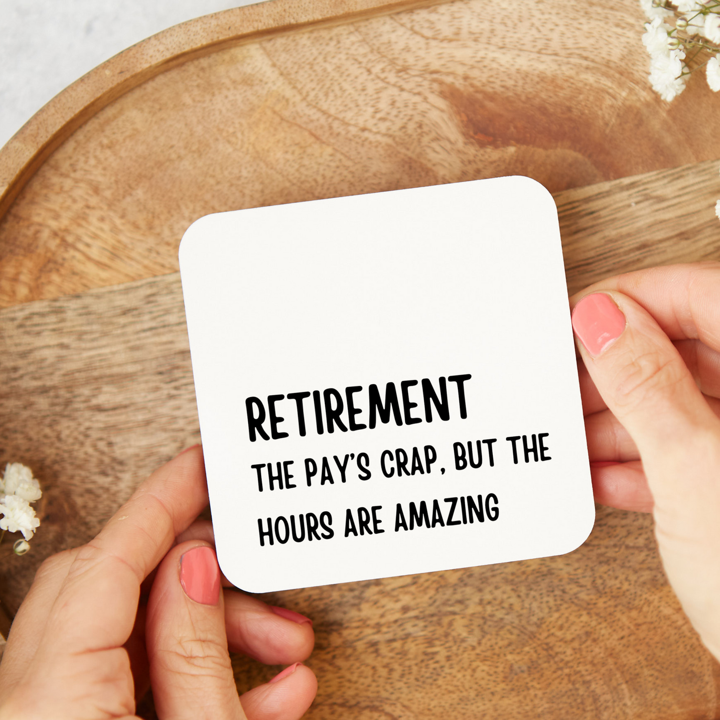 Coaster with humorous retirement message held by hands on a wooden surface