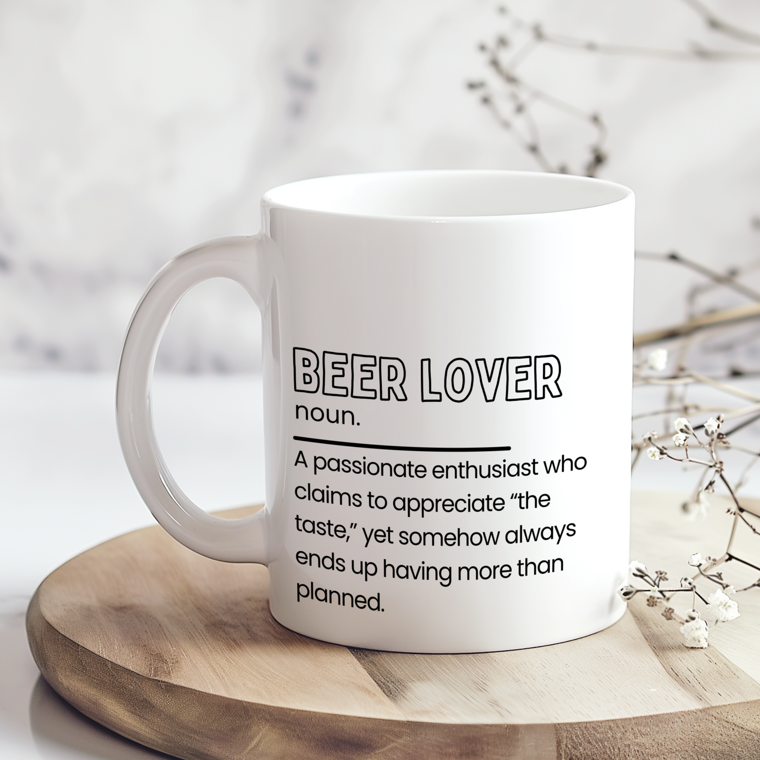 White ceramic mug with “Beer Lover noun.” definition style design in black typography, featuring a funny quote about appreciating the taste but always drinking more than planned, displayed on a neutral wooden surface.