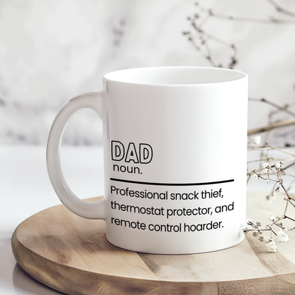 White ceramic mug with funny dad definition quote reading “Professional snack thief, thermostat protector, and remote control hoarder,” displayed on wooden board in neutral styled mockup, humorous Father’s Day gift for dads.