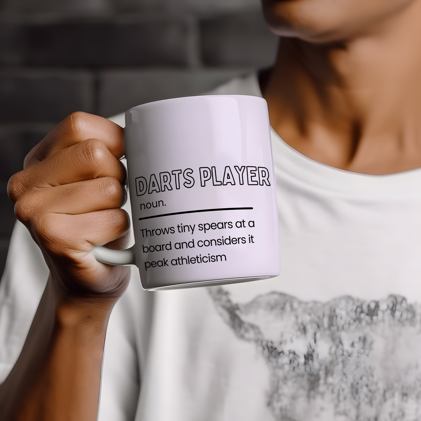 White ceramic mug featuring a humorous "Darts Player" definition with the slogan "Throws tiny spears at a board and considers it peak athleticism", making a funny gift for darts lovers.