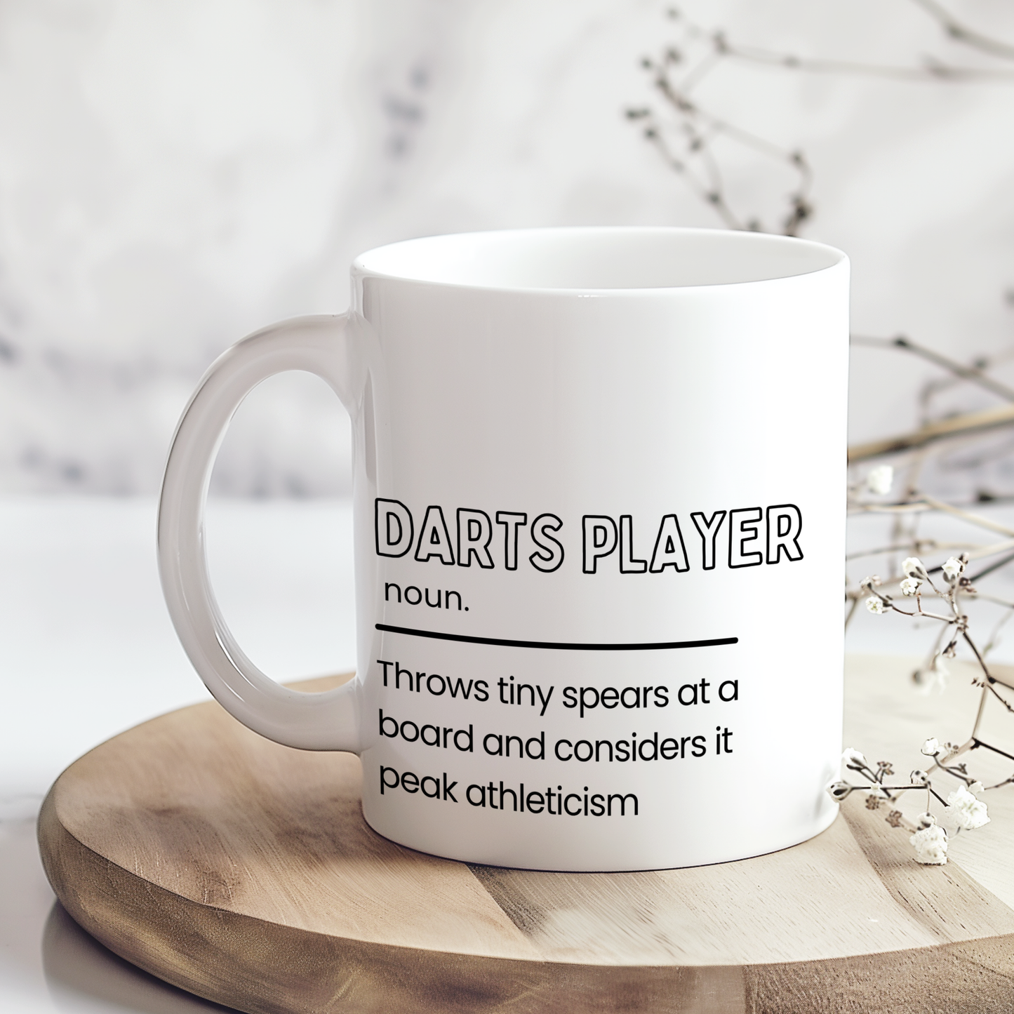 White ceramic mug featuring a humorous "Darts Player" definition with the slogan "Throws tiny spears at a board and considers it peak athleticism", making a funny gift for darts lovers.