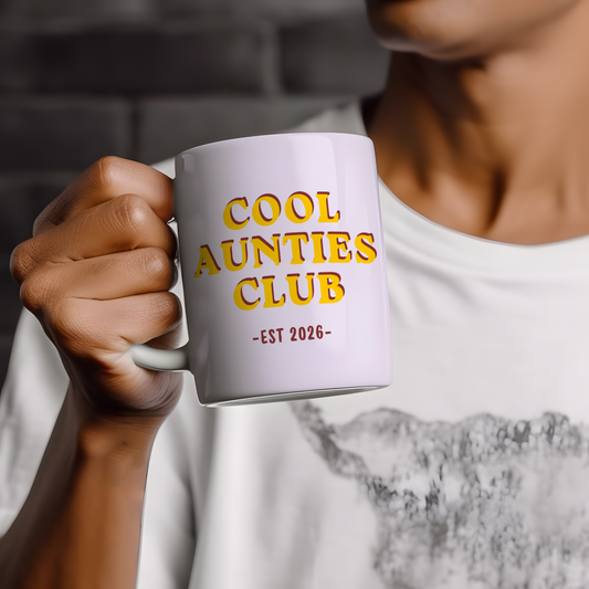 White ceramic mug featuring “Cool Aunties Club EST 2026” retro style typography in yellow and red colours, displayed on a neutral wooden background with minimalist styling.