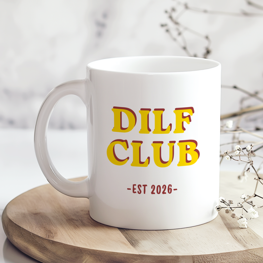 White ceramic mug featuring “DILF Club EST 2026” retro style typography in yellow and red colours, displayed on a neutral wooden background with minimalist styling.