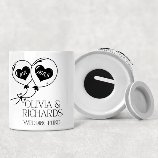 Personalised ceramic wedding fund money box with custom names and date, ideal engagement gift or bridal shower present, white pot with elegant lettering and heart detail.