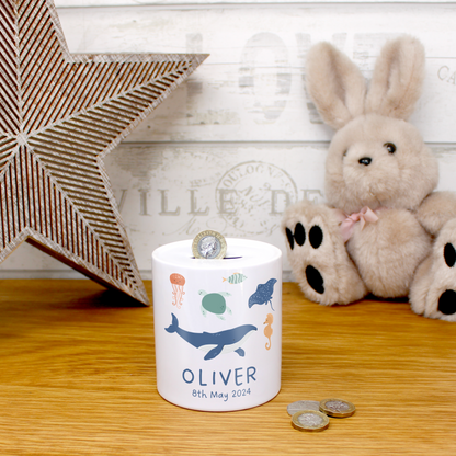Personalized children's piggy bank with coins and a plush toy on a wooden surface.