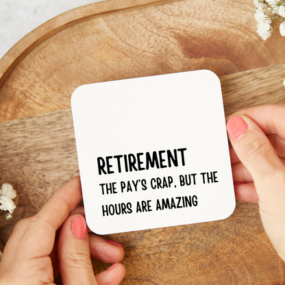 Coaster with humorous retirement message held by hands on a wooden surface