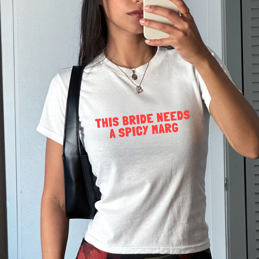 White fitted baby tee with “This Bride Needs a Spicy Marg” slogan in bold bridal typography, styled for a hen party outfit.