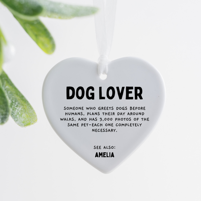 white ceramic heart ornament with dog lover definition text hanging with white ribbon on wooden tray beside pink rose