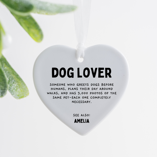 white ceramic heart ornament with dog lover definition text hanging with white ribbon on wooden tray beside pink rose