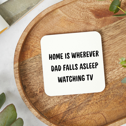 White ceramic mug with the funny quote “Home Is Wherever Dad Falls Asleep Watching TV” in bold black text, held in hand lifestyle mockup, humorous Father’s Day gift mug for dads who nap watching television.