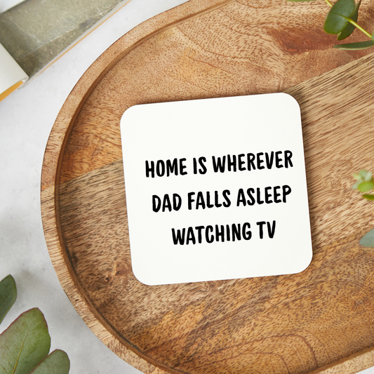 White ceramic mug with the funny quote “Home Is Wherever Dad Falls Asleep Watching TV” in bold black text, held in hand lifestyle mockup, humorous Father’s Day gift mug for dads who nap watching television.