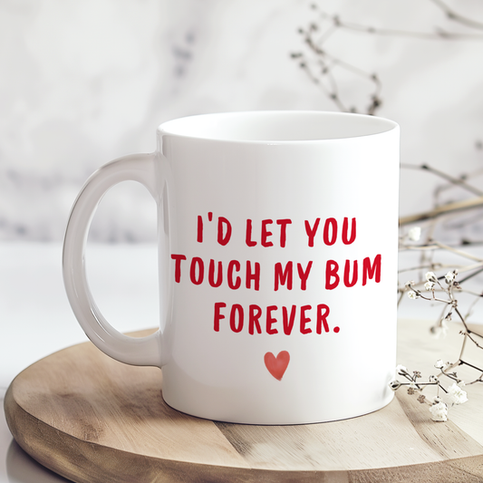 White glossy ceramic mug with funny “I’ll Let You Touch My Bum Forever” text printed on both sides, cheeky Valentine’s Day gift for couples.