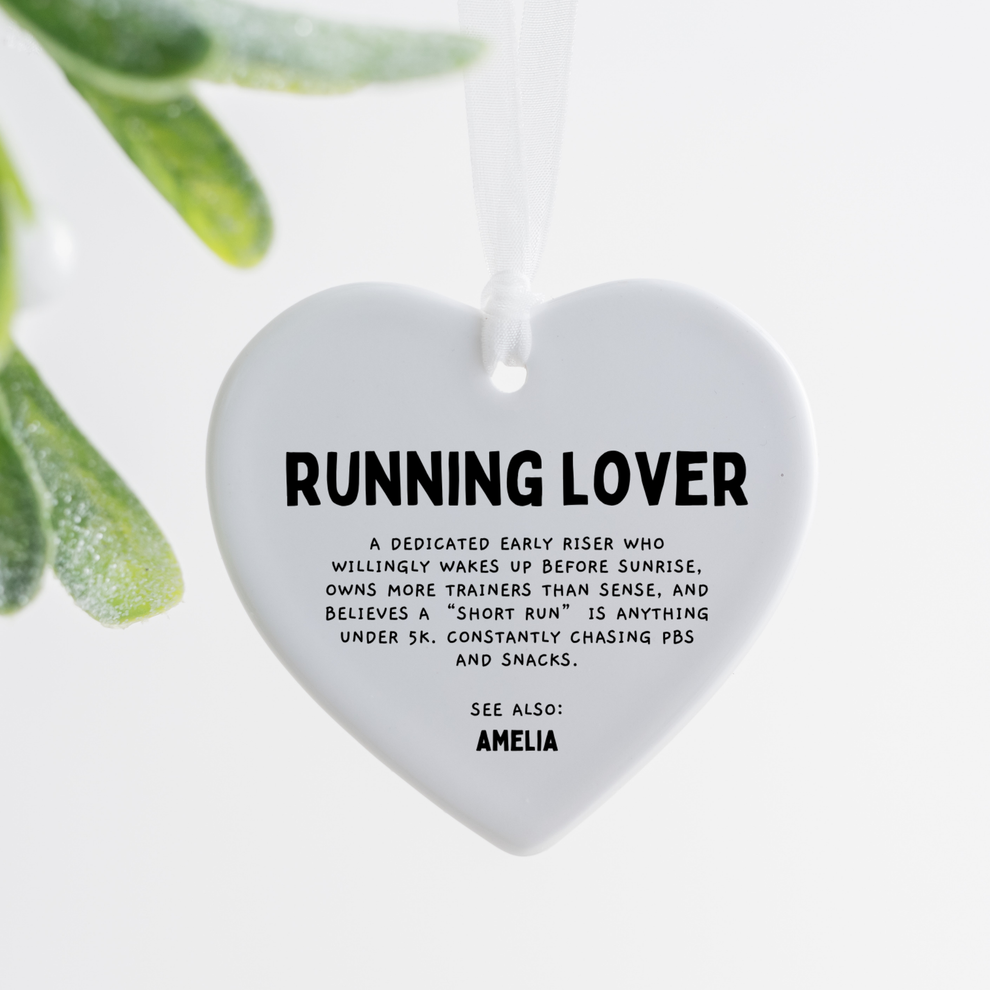 white ceramic heart ornament with running lover definition text hanging with white ribbon on wooden tray with pink rose