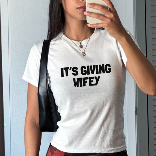 White fitted baby tee featuring the slogan “It’s Giving Wifey” in modern bridal typography, styled as a hen party outfit.